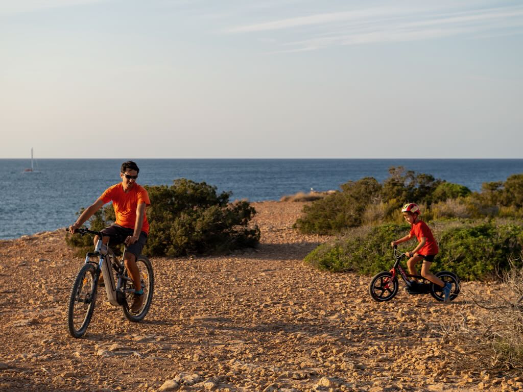 Padre e hijo en bicicleta por un camino de tierra junto a la costa de Ibiza al atardecer