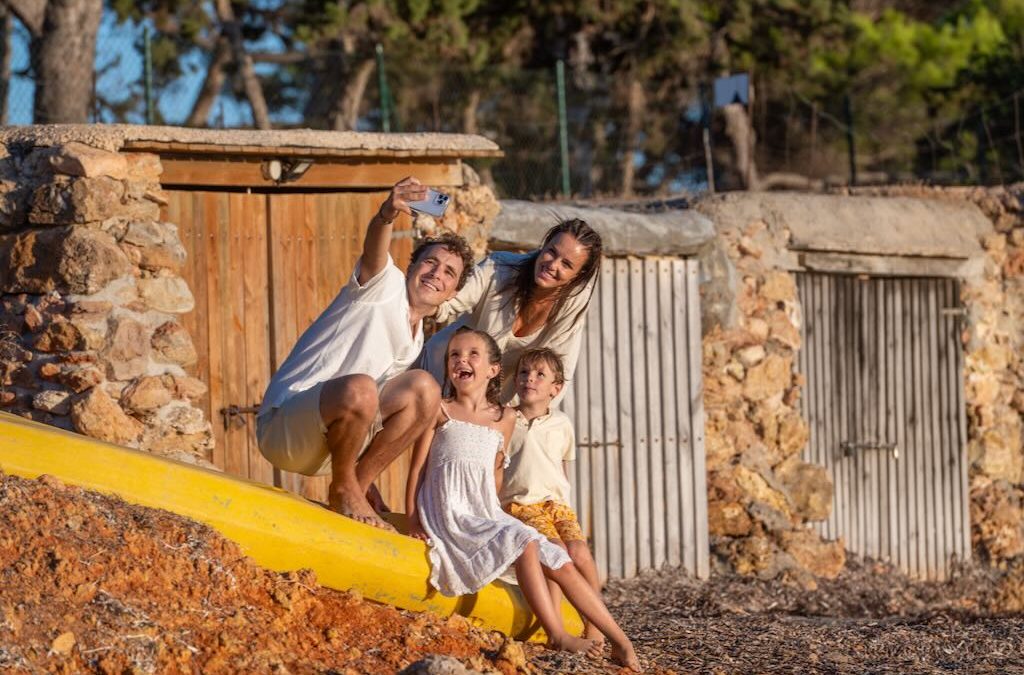 Familia con dos hijos haciéndose un selfie junto a las casetas de piedra de una cala de Ibiza al atardecer