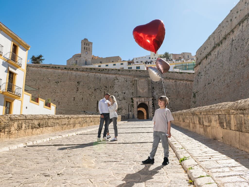 Familia con niño y globos en forma de corazón frente a las murallas de Dalt Vila, Ibiza